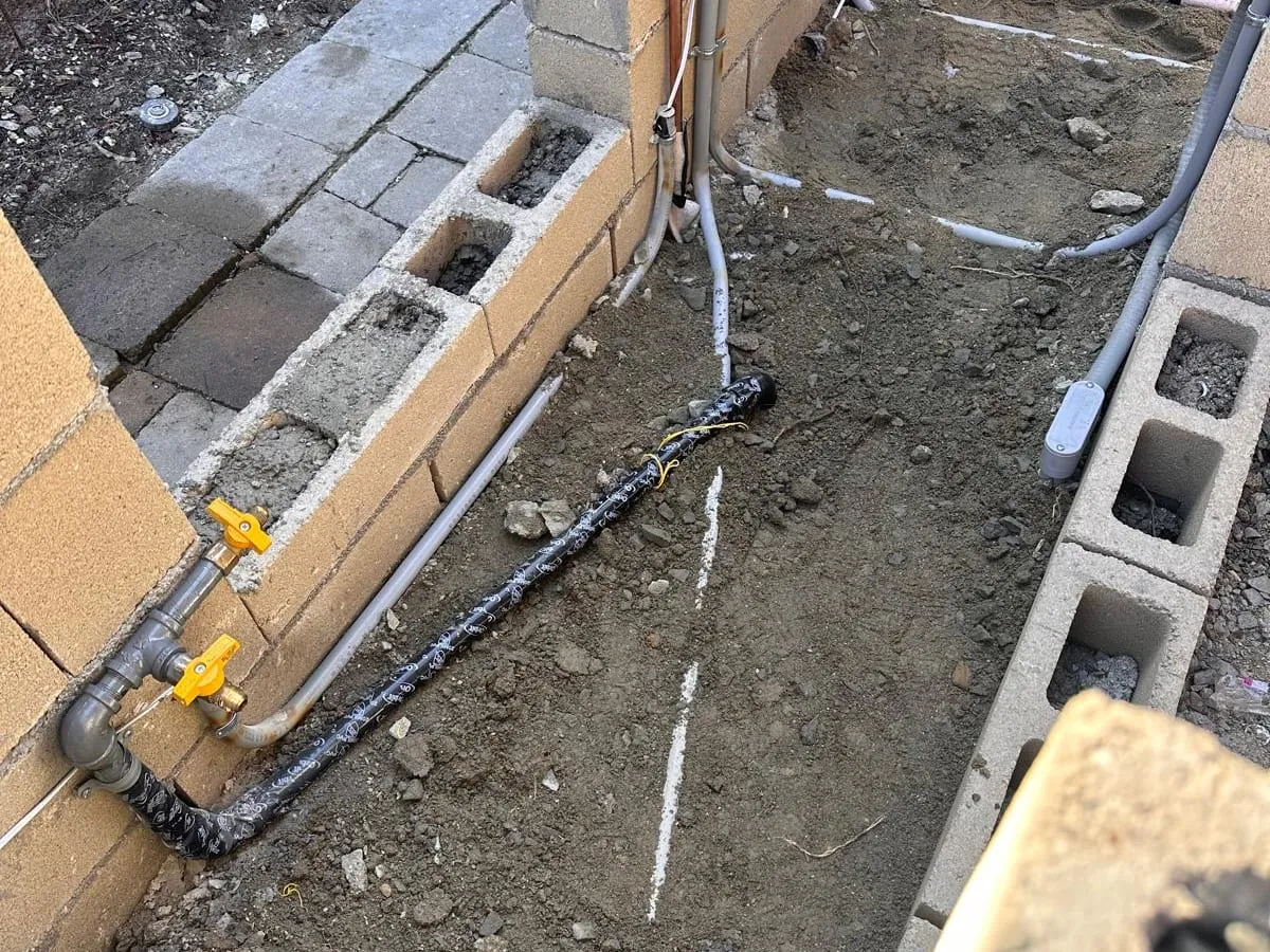 Gas pipe with two yellow-handled shutoff valves along a new block wall, next to copper water lines and electrical conduit