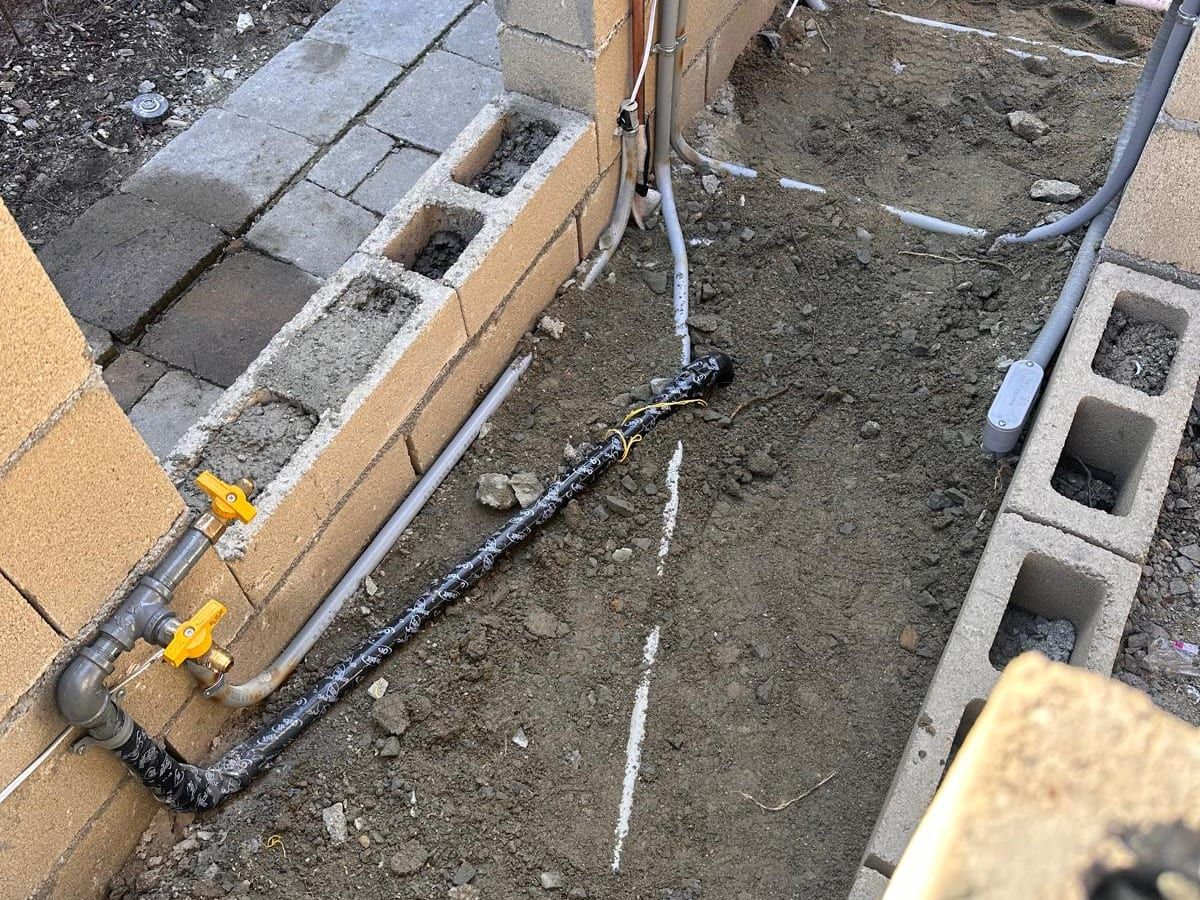 Gas pipe with two yellow-handled shutoff valves along a new block wall, next to copper water lines and electrical conduit